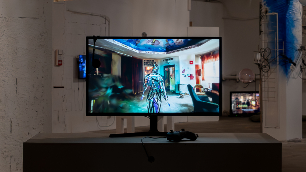 SAMPLE(S) v.1 — interactive installation, Krypta exhibition, October 2024, Le Sample, Bagnolet - A monitor displaying a digital art piece with an abstract character in a room, accompanied by a gaming controller, set in an art exhibition space.