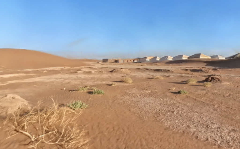 3DGS Morocco - A barren desert landscape with sand dunes in the background and several tents on flat ground under a clear blue sky.